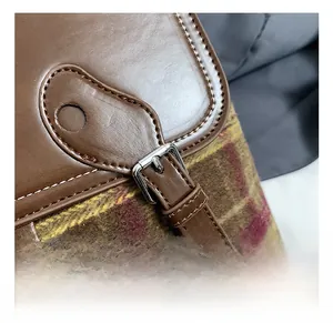 Dettaglio macro della fibbia in argento su zaino in pelle marrone e plaid