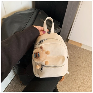 Detail van een crème canvas mini-rugzak met zilveren metalen ritsen en een bruine pluche hanger