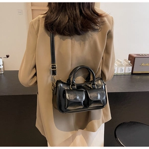 Detail of black glossy Boston bag featuring double front flap pockets and gold hardware