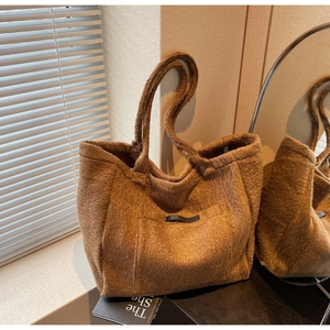 Detail of dark brown plush tote bag with black leather trim in warm indoor lighting