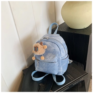 Detail van een lichtblauwe denim mini-rugzak met een bruine pluche schaapshanger eraan