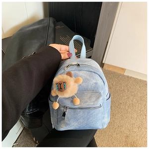 Detail van blauwe denim mini rugzak met bruine pluchen dierenhanger en lederen handvat
