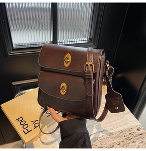 Detail view of a vintage dark brown crossbody bag featuring dual gold twist lock buckles