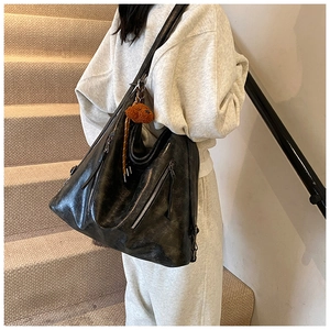 Close-up of black tote bag with vintage texture, zipper detail, and small plush pendant