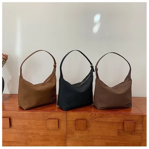 Trois sacs hobo minimalistes en caramel, noir et marron exposés sur une étagère en bois