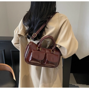 Detail of reddish-brown glossy leather crossbody bag with dual front pockets and gold hardware