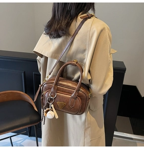 Sac bandoulière vintage en cuir marron avec charm de baseball porté sur un trench-coat