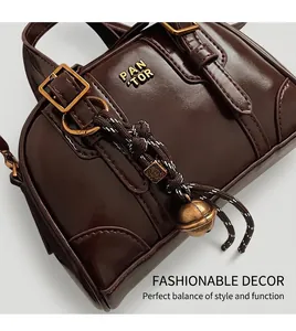Macro shot of dark brown glossy leather bag with gold logo and vintage bell charm