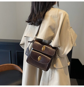 Detail of dark brown crossbody bag with two front pockets and gold metallic buckles