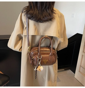 Sac bandoulière en cuir marron avec breloques porté par une femme en trench-coat