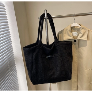 Detail of black faux shearling tote bag with leather straps hanging on a metal hanger