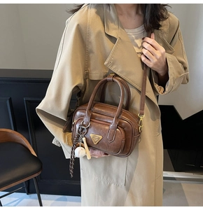 Sac Boston marron avec pendentif de baseball et plaque en métal sur un trench-coat beige