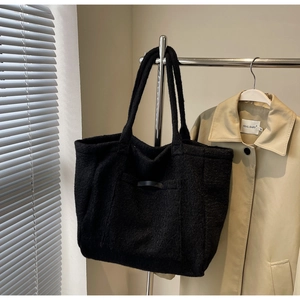 Detailed close-up of a black textured fuzzy tote bag featuring a front pocket and leather trim