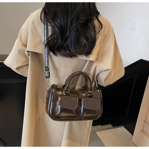 Detail of dark brown glossy leather handbag worn with a beige trench coat on model