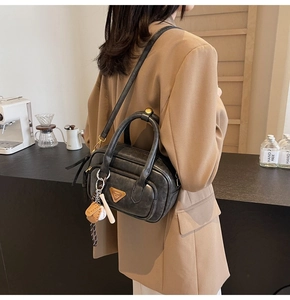 Détail du sac bandoulière noir avec breloque de baseball et plaque logo en métal
