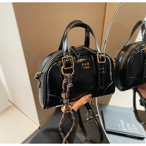 Close-up of black glossy patent leather handbag with gold logo and woven rope detail