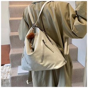 Detailed side view of a large cream faux leather tote bag worn by a model in a green coat