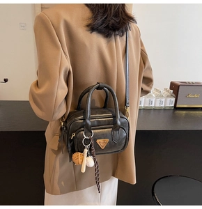 Détail d'un sac bandoulière noir avec breloque de baseball sur un costume marron