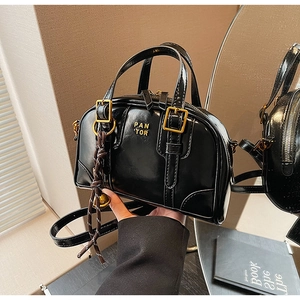 Detail of glossy black Boston bag with gold hardware and brand lettering