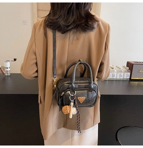 Détail du sac à main en cuir noir avec logo triangulaire vintage et breloques de sport