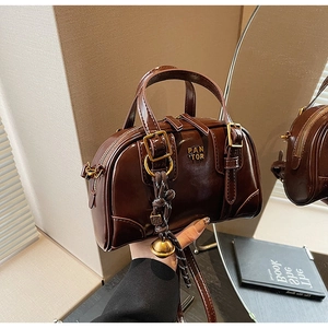 Detail of dark brown glossy patent leather bag with gold buckle and brand logo