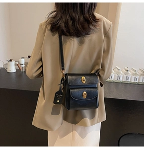 Detail of black vintage crossbody bag with dual golden turn-lock buckles on a model