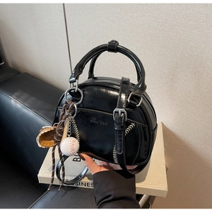 Detail einer schwarzen Lackhandtasche mit weißen Nähten und Mini-Baseball-Anhänger