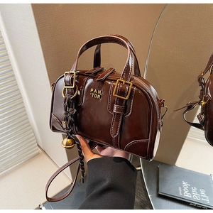 Detail of vintage brown patent leather handbag with gold metal logo and tassel charm