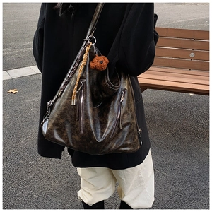 Brown vintage leather tote bag shown on model featuring decorative zippers and bear pendant