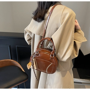 Braune Leder-Bowlingtasche mit weißen Nähten und Baseball-Anhänger zum Trenchcoat