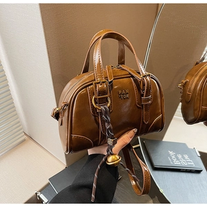 Close-up of deep brown leather Boston bag with PAN TOR logo and gold bell charm detail