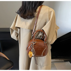 Details der kaffeebraunen Bowlingtasche aus Leder mit weißen V-Nähten und Tieranhänger