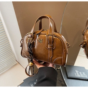 Detailed view of brown retro Boston bag with metal logo and woven ball charm decoration