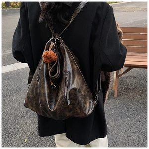 Detail view of deep brown oily wax leather backpack with plush ball charm on a wooden bench