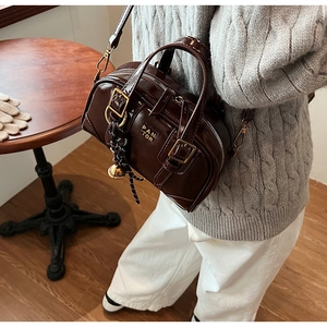 Close-up of a dark brown glossy leather Boston bag with gold hardware and woven lanyard
