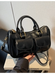 Glossy black Boston handbag with gold hardware and dual front pockets on display