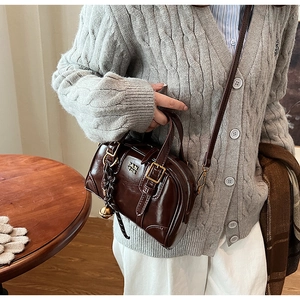 Detail of a dark brown glossy leather Boston bag with gold buckle and a metal charm