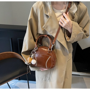 Detail der braunen Leder-Bowlingtasche mit Baseball-Nähten und Mini-Handschuh-Anhänger