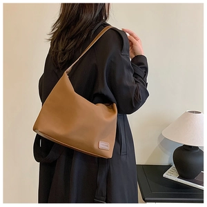 Gros plan d'un sac porté épaule caramel avec logo rectangulaire sur une surface minimaliste