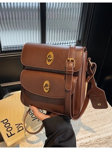 Vintage brown leather crossbody bag with double gold twist locks on beige marble stone