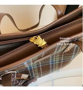 Detail of a smooth metal zipper with a golden bear charm on a plaid tote bag