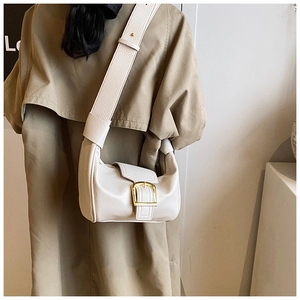 Dettaglio borsa a tracolla crema in pelle con fibbia dorata su un trench beige