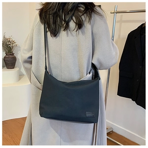 Détail du sac hobo en nylon noir avec écusson en cuir porté sur un manteau en laine