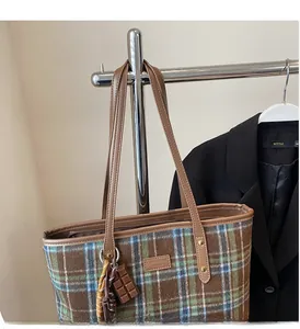 Detail of plaid tote bag with brown leather handles and golden rivet reinforcements