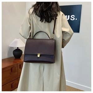 Detail shot of a vintage brown leather crossbody bag styled with a beige trench coat