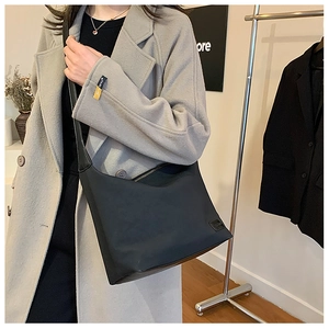 Détail du sac bandoulière en nylon noir avec logo porté sur un manteau de laine gris