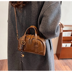 Detail of a brown leather crossbody bag with metal PAN TOR logo and buckle straps