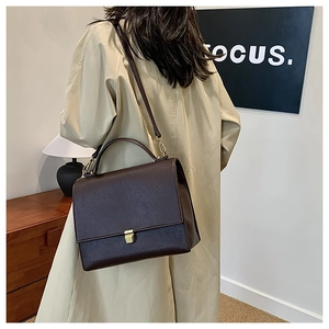 Detail view of dark brown pebbled leather crossbody bag on beige trench coat outfit