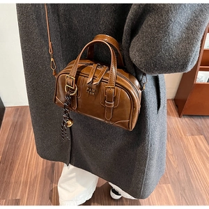 Close-up of a brown leather boston bag with top handles, crossbody strap, and woven charm