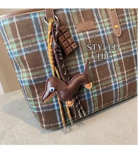 Detail of dachshund leather charm and chocolate pendant on a brown plaid tote bag